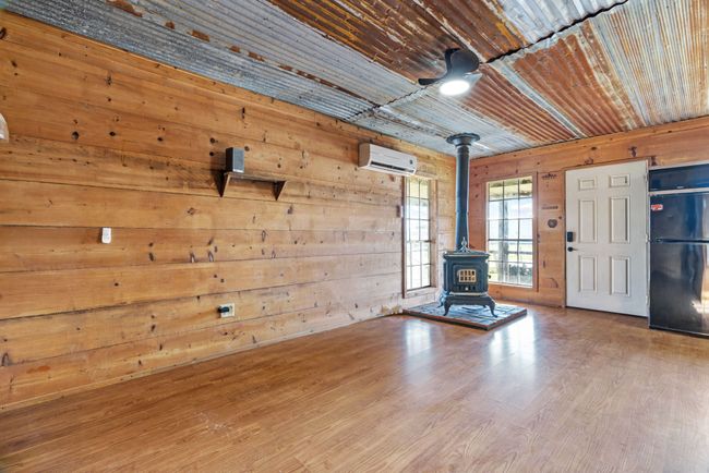 Unfurnished living room with a wall mounted air conditioner, a wood stove, wood walls, and wood finished floors | Image 14