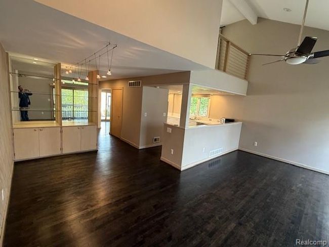 Unfurnished living room featuring dark wood-style floors, healthy amount of natural light, high vaulted ceiling, ceiling fan, and beam ceiling | Image 11
