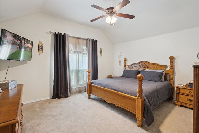 Primary bedroom featuring lofted ceiling, light colored carpet, a ceiling fan, and baseboards | Image 21