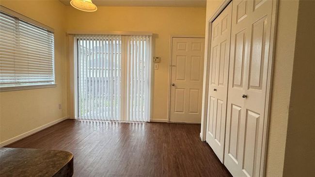 Bright room with wood flooring, large windows with blinds, sliding glass door leading outside, and ample closet space. Ideal for a cozy living area or home office. | Image 10