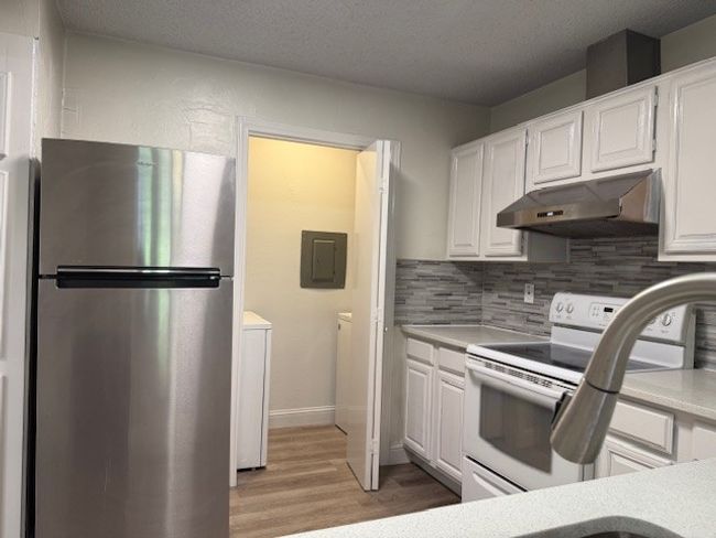 Kitchen featuring freestanding refrigerator, under cabinet range hood, electric range, electric panel, and separate washer and dryer | Image 18