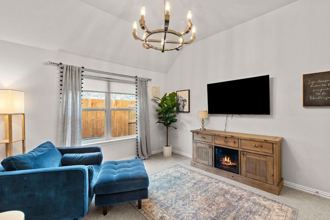 Carpeted living room featuring a chandelier, vaulted ceiling, baseboards, and a warm lit fireplace | Image 17