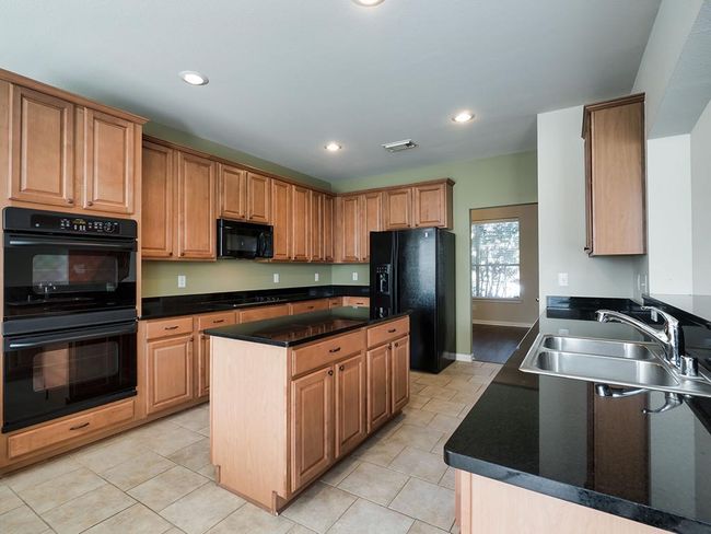 Kitchen featuring black appliances, a sink, dark countertops, a center island, and light tile patterned floors | Image 21