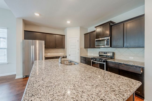 Kitchen with dark brown cabinets, appliances with stainless steel finishes, light stone counters, a sink, and a kitchen island with sink | Image 6