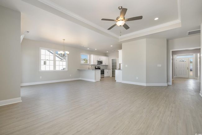 Unfurnished living room with sink, a raised ceiling, light hardwood / wood-style flooring, ceiling fan with notable chandelier, and ornamental molding | Image 8