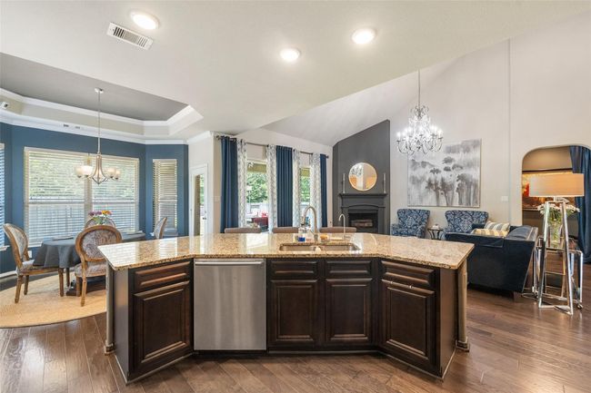 This inviting open-concept space features a modern kitchen with a large island and granite countertops, seamlessly flowing into a cozy living area with a fireplace. The dining area is bright with natural light from multiple large windows, and elegant chandeliers add a touch of luxury. | Image 8