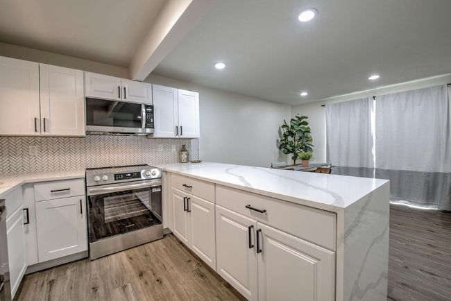 Kitchen featuring light wood-style flooring, white cabinets, appliances with stainless steel finishes, a peninsula, and backsplash | Image 14