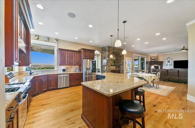 Kitchen featuring a fireplace, appliances with stainless steel finishes, ceiling fan, light wood-type flooring, and a kitchen breakfast bar | Image 11