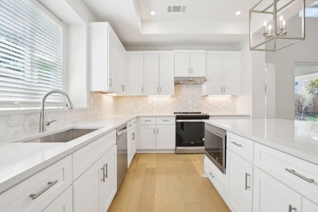 Kitchen with visible vents, a chandelier, under cabinet range hood, a sink, and stainless steel appliances | Image 17