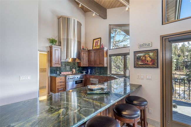 Kitchen with double oven range, backsplash, a kitchen breakfast bar, dark stone counters, and range hood | Image 14