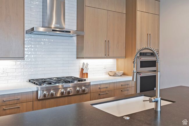 Kitchen featuring wall chimney exhaust hood, stainless steel appliances, modern cabinets, and decorative backsplash | Image 10