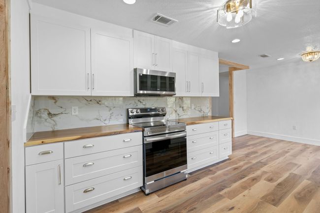 Kitchen with butcher block counters, light wood-style floors, visible vents, decorative backsplash, and stainless steel appliances | Image 25
