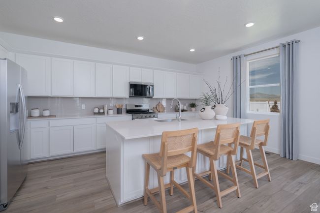 Kitchen featuring stainless steel appliances, light wood finished floors, tasteful backsplash, white cabinets, and a kitchen island with sink | Image 17