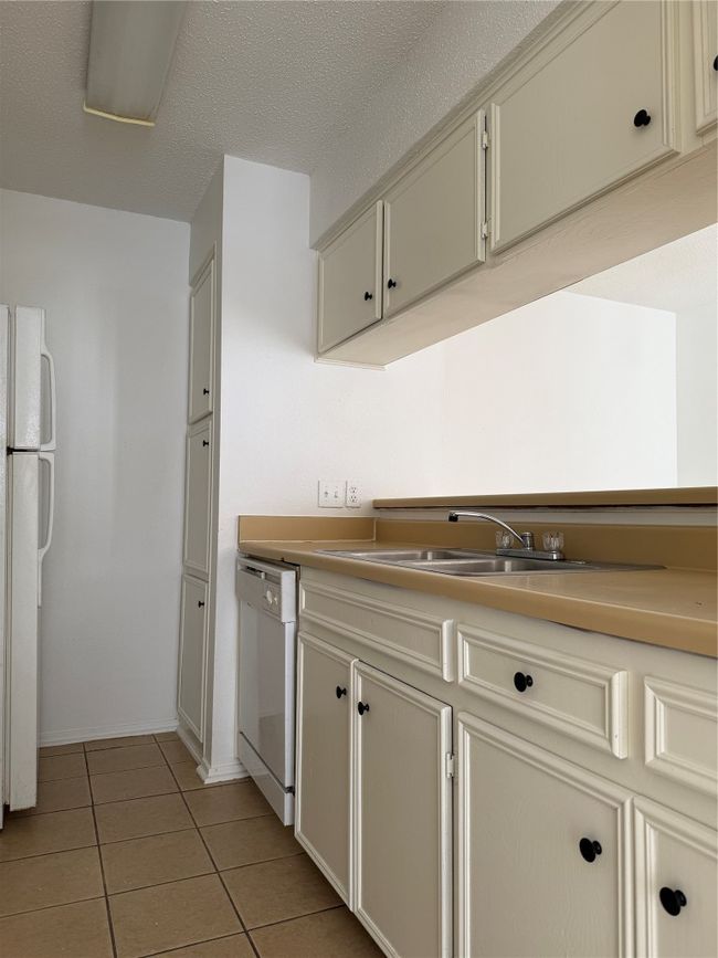 Kitchen with dishwashing machine, refrigerator, light tile patterned flooring, a sink, and a textured ceiling | Image 6