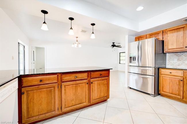 Kitchen featuring brown cabinets, decorative backsplash, white dishwasher, light tile patterned flooring, and stainless steel fridge | Image 16