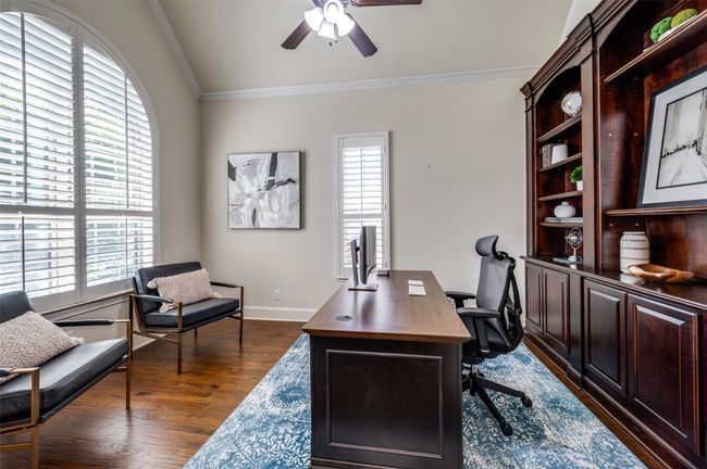 he bright and airy office boasts oversized curved windows adorned with plantation shutters, while rich hand-scraped wood floors and deep brown built-in cabinets lend a stately, refined feel. Don’t miss the impressive vaulted ceiling with elegant crown molding, adding a touch of sophistication. | Image 4