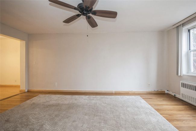 Empty room featuring radiator heating unit, light wood finished floors, and ceiling fan | Image 4