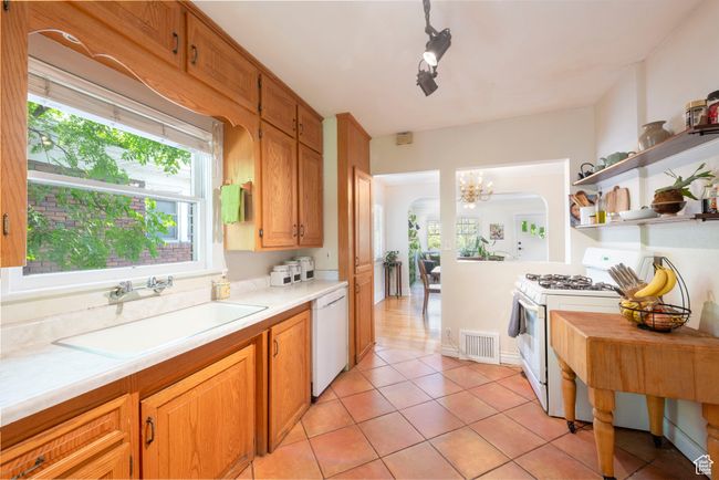 Kitchen with white appliances, light countertops, light tile patterned floors, open shelves, and a chandelier | Image 12