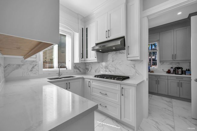 Kitchen with under cabinet range hood, stainless steel gas cooktop, tasteful backsplash, light marble finish flooring, and white cabinetry | Image 11