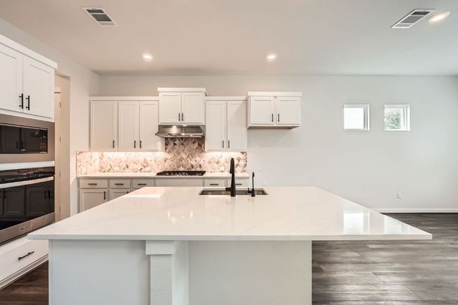 Kitchen with stainless steel appliances, a sink, under cabinet range hood, tasteful backsplash, and an island with sink | Image 8