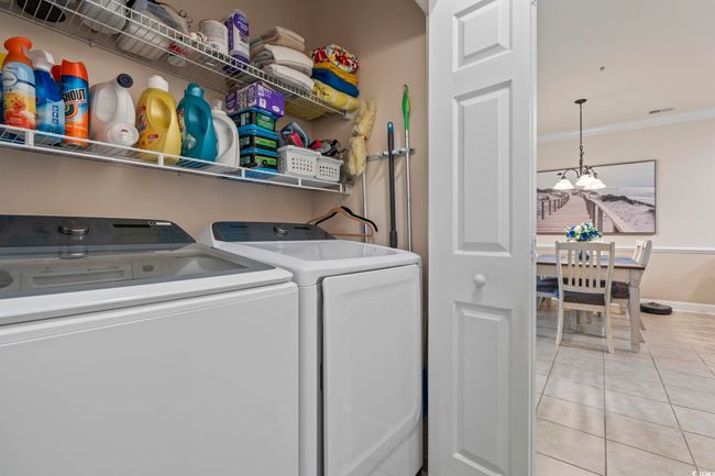 Laundry area featuring washer and clothes dryer, crown molding, light tile patterned floors, and a chandelier | Image 9
