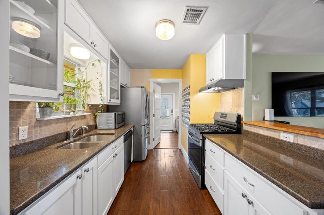 Kitchen featuring appliances with stainless steel finishes, glass insert cabinets, white cabinets, dark wood-style flooring, and dark stone counters | Image 8