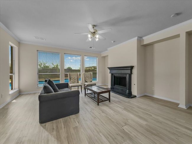 Living room with ornamental molding, a fireplace with raised hearth, ceiling fan, and light wood-type flooring | Image 6