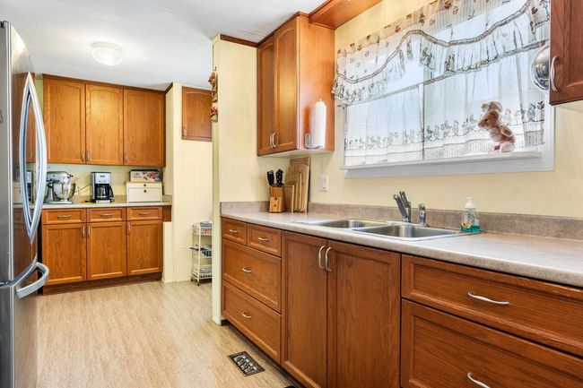 Kitchen with light countertops, light wood-style flooring, brown cabinets, a sink, and freestanding refrigerator | Image 14