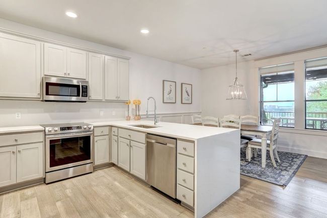 Kitchen with appliances with stainless steel finishes, a sink, a peninsula, light wood finished floors, and light countertops | Image 7