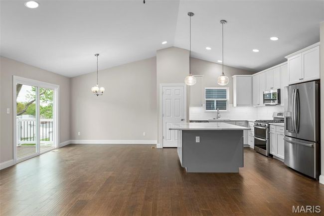 Kitchen with stainless steel appliances, a kitchen island, a chandelier, baseboards, and white cabinets | Image 15