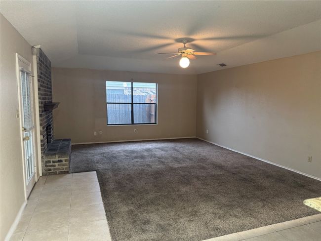 Unfurnished living room featuring carpet, a ceiling fan, a fireplace, tile patterned floors, and visible vents | Image 4