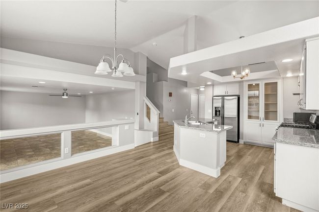 Kitchen with a sink, a center island with sink, light wood-style floors, white cabinetry, and stainless steel refrigerator with ice dispenser | Image 13