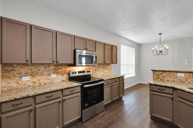 Kitchen featuring stainless steel appliances, a textured ceiling, decorative backsplash, dark wood-type flooring, and a chandelier | Image 12