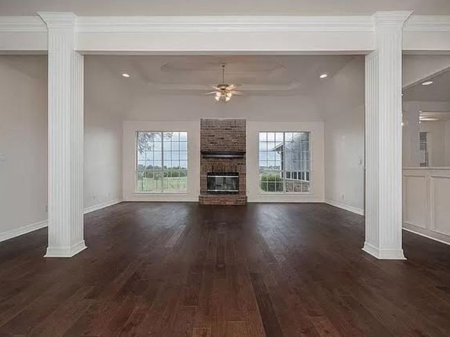 Unfurnished living room featuring decorative columns, healthy amount of natural light, ceiling fan, dark wood-style flooring, and ornamental molding | Image 5