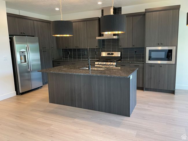 Kitchen with appliances with stainless steel finishes, modern cabinets, a textured ceiling, a center island with sink, and dark stone countertops | Image 5