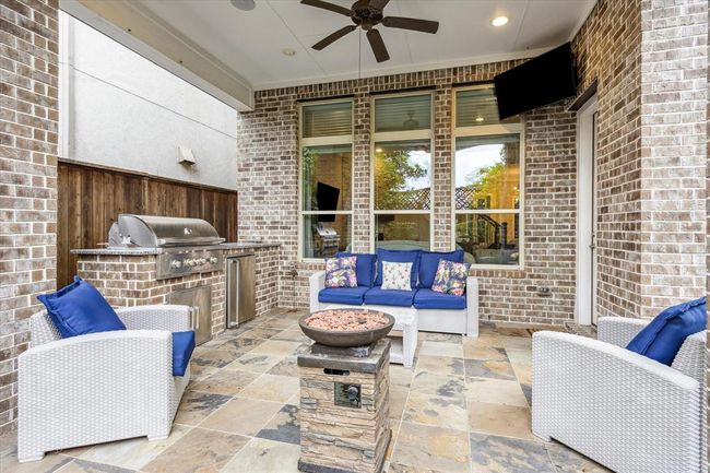 This outdoor patio has space for a sitting area and a dining table. The built-in grill is ready to go! Notice the brick walls, ceiling fan, and mounted TV, ideal for entertaining. | Image 33