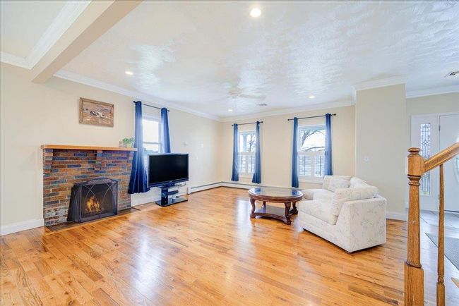 Living area featuring a healthy amount of sunlight, a fireplace, crown molding, and wood finished floors | Image 8