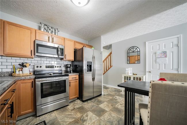 Kitchen with backsplash, appliances with stainless steel finishes, dark tile patterned flooring, and a textured ceiling | Image 7