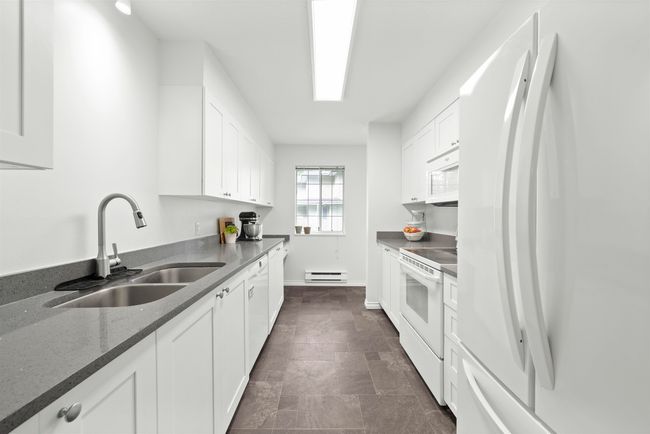 Kitchen featuring baseboard heating, white appliances, white cabinetry, dark stone counters, and a sink | Image 11