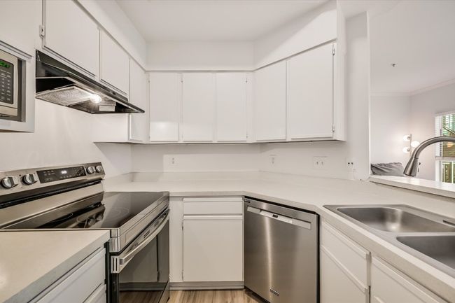Kitchen featuring appliances with stainless steel finishes, under cabinet range hood, white cabinetry, light countertops, and light wood-type flooring | Image 4