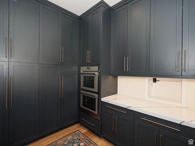 Kitchen with stainless steel double oven, light wood-type flooring, light stone counters, and dark cabinetry | Image 42