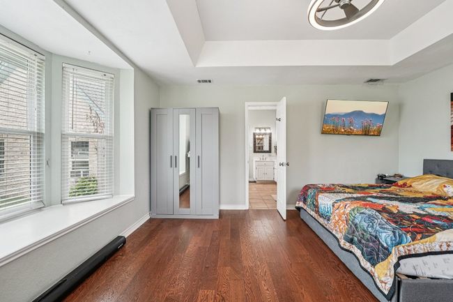 Bedroom with baseboard heating, wood finished floors, multiple windows, and a tray ceiling | Image 16