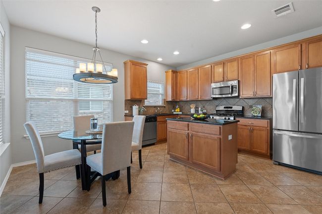 Kitchen with appliances with stainless steel finishes, dark countertops, tasteful backsplash, a chandelier, and a kitchen island | Image 14