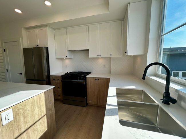 Kitchen with white cabinetry, a sink, freestanding refrigerator, wood finished floors, and black range with gas cooktop | Image 4