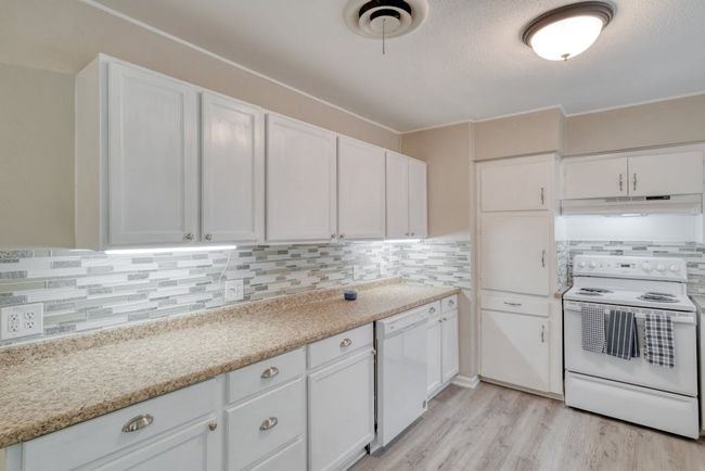 Kitchen featuring light wood-style flooring, under cabinet range hood, white appliances, white cabinetry, and decorative backsplash | Image 12