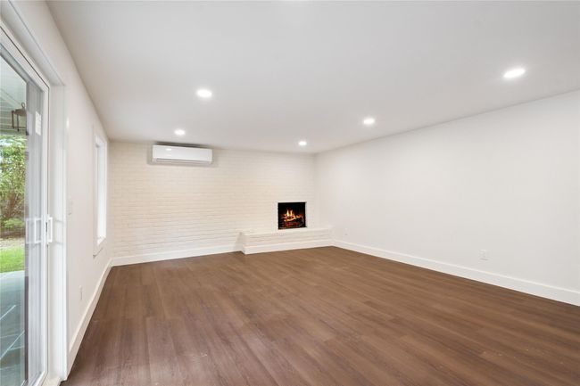Unfurnished living room with a wall mounted AC, dark wood-type flooring, a brick fireplace, recessed lighting, and brick wall | Image 30