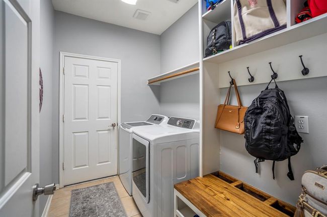 The downstairs laundry room features a custom-built mud bench with hooks and cubby spaces, providing a perfect spot for coats, bags, and shoes. The convenient doorway leads directly to the garage for easy access. | Image 31