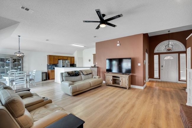 Living area featuring ceiling fan, light wood-type flooring, a textured ceiling, lofted ceiling, and a chandelier | Image 6