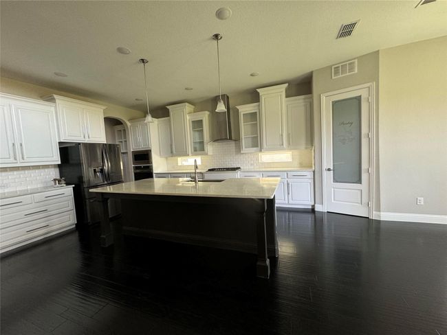 Kitchen featuring wall chimney range hood, stainless steel appliances, tasteful backsplash, white cabinetry, and recessed lighting | Image 4