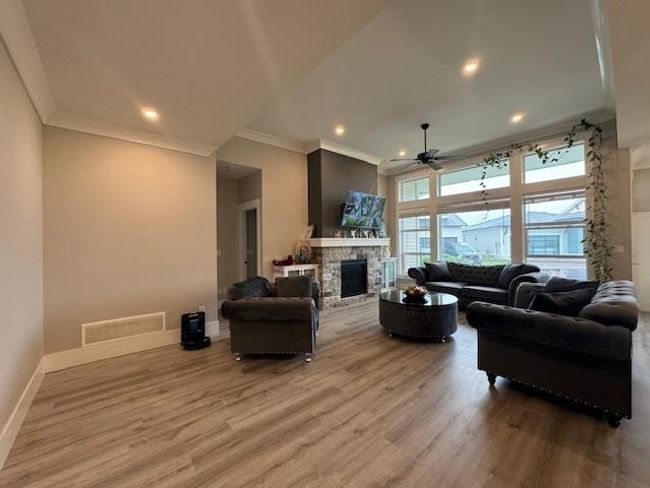 Living room featuring a ceiling fan, wood finished floors, a fireplace, baseboards, and visible vents | Image 18